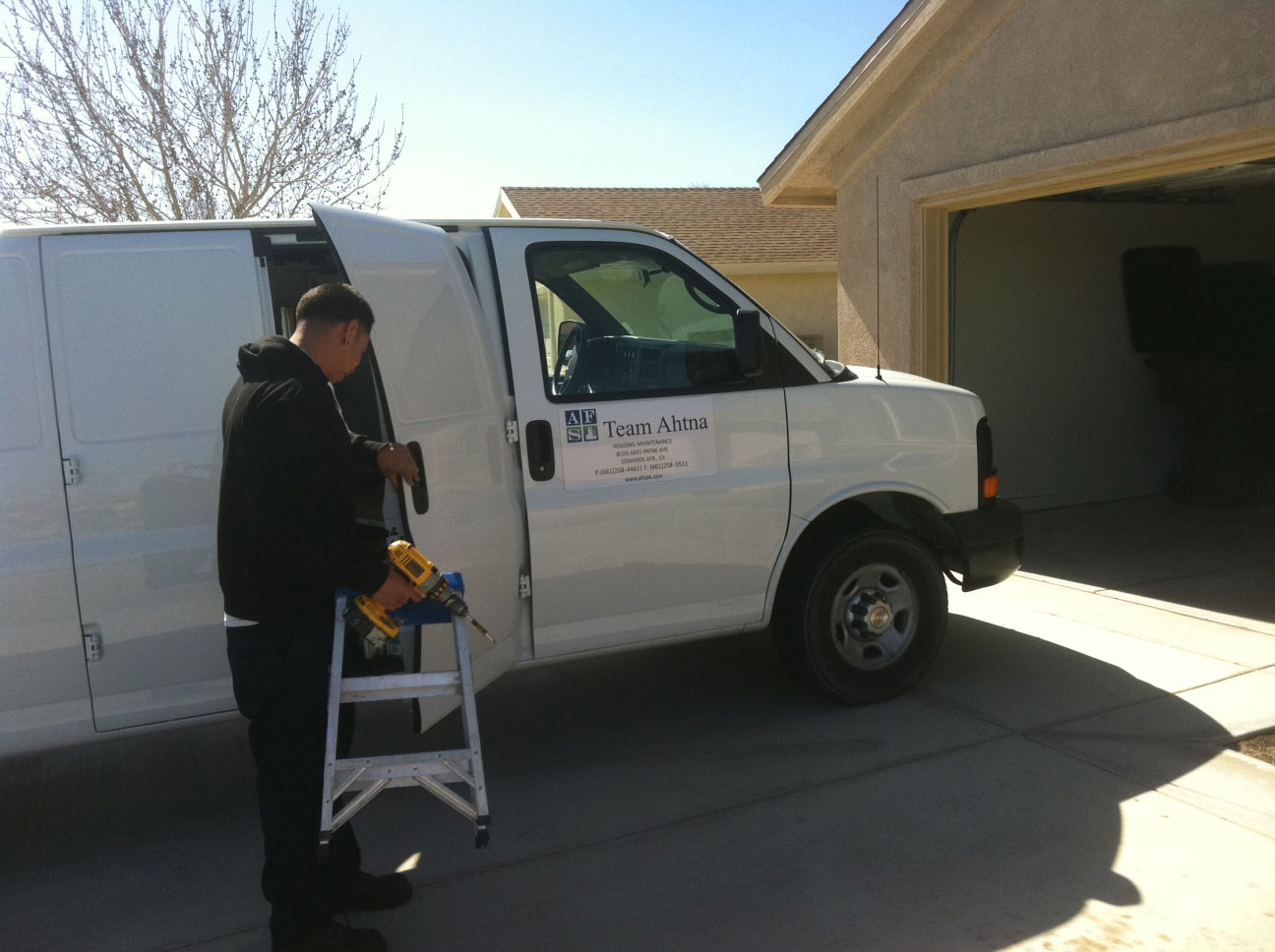 Man with step ladder and drill stepping out of work van